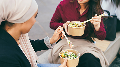 Zwei Frauen teilen sich eine Mahlzeit, essen mit Plastikbesteck und Pappschüssel